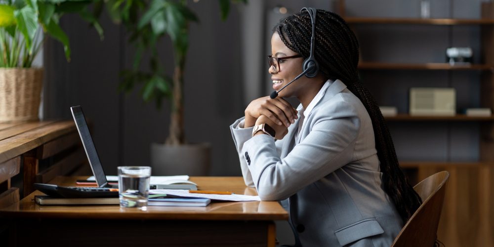 Friendly afro woman remote callcenter worker in headset with microphone communicating with customers