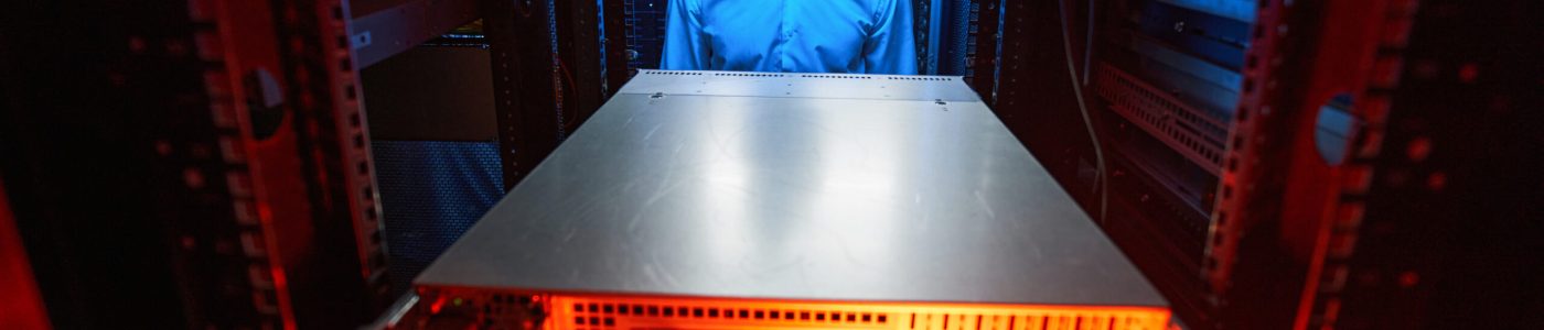 Server technician in data retention facility standing on aisle between server racks
